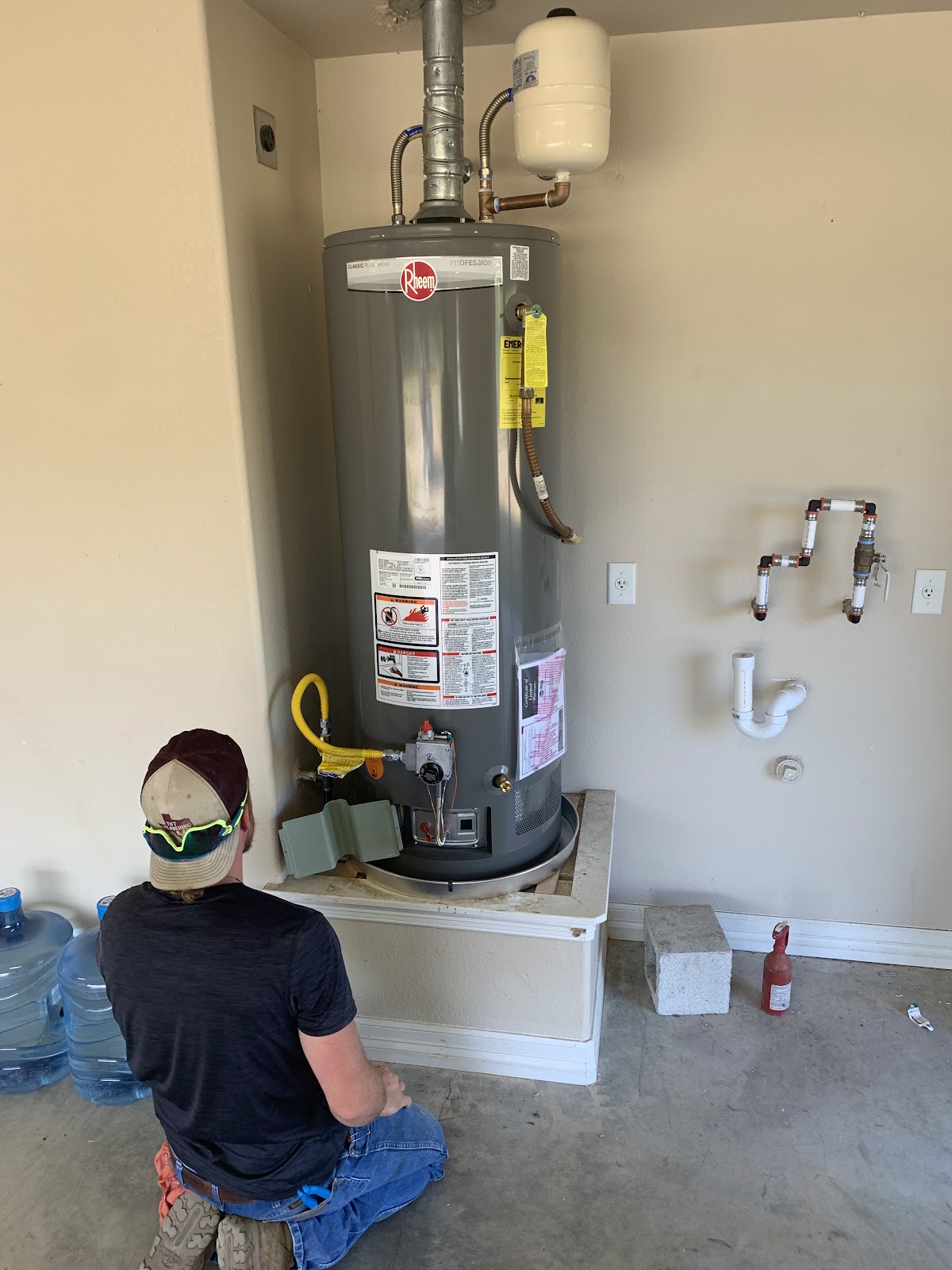 TNT Plumbing technician working on a Rheem water heater installation in a garage