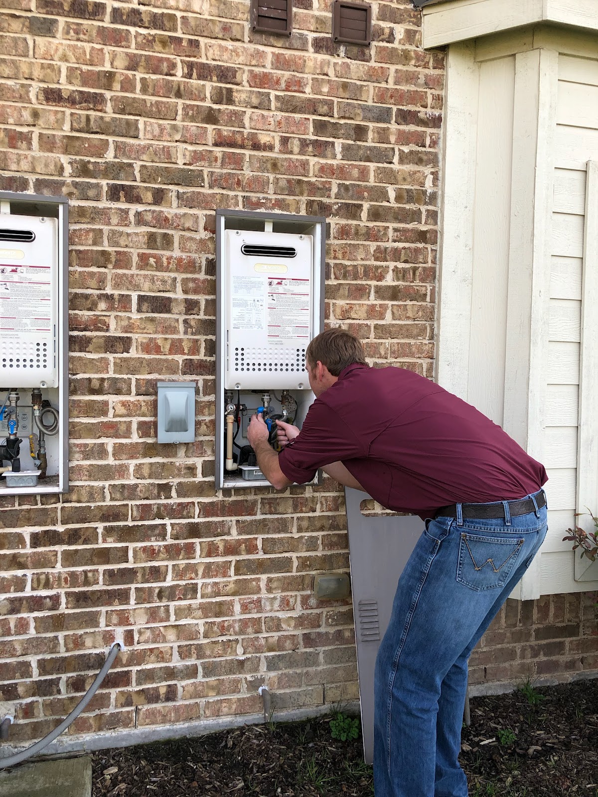 TNT technician installing tankless water heaters on an exterior brick wall